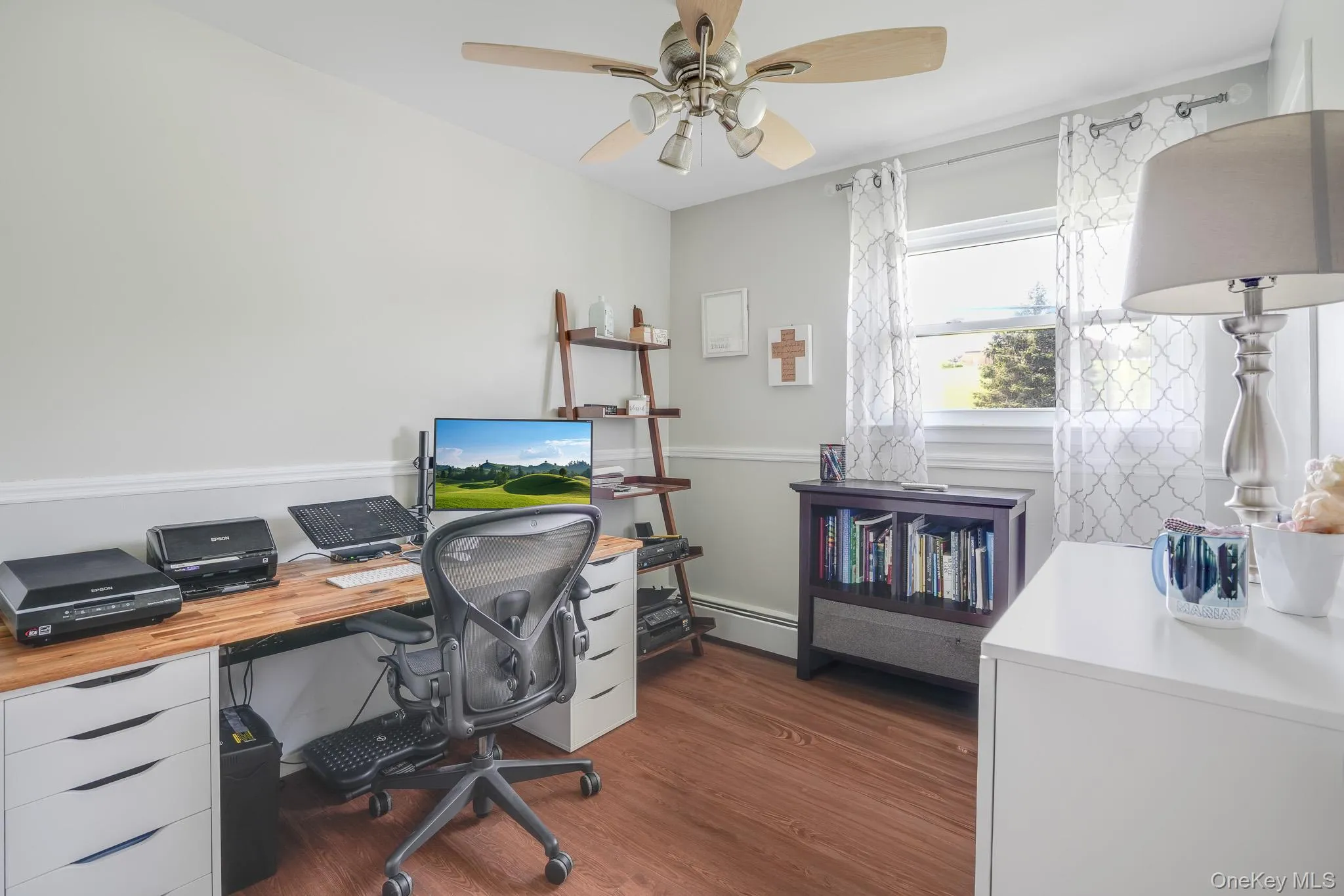 Wood-finish flooring throughout, featuring a ceiling fan with integrated lighting, a window with natural light, and a chair rail molding Wood-finish flooring throughout, featuring a ceiling fan with integrated lighting, a window with natural light, and a chair rail molding