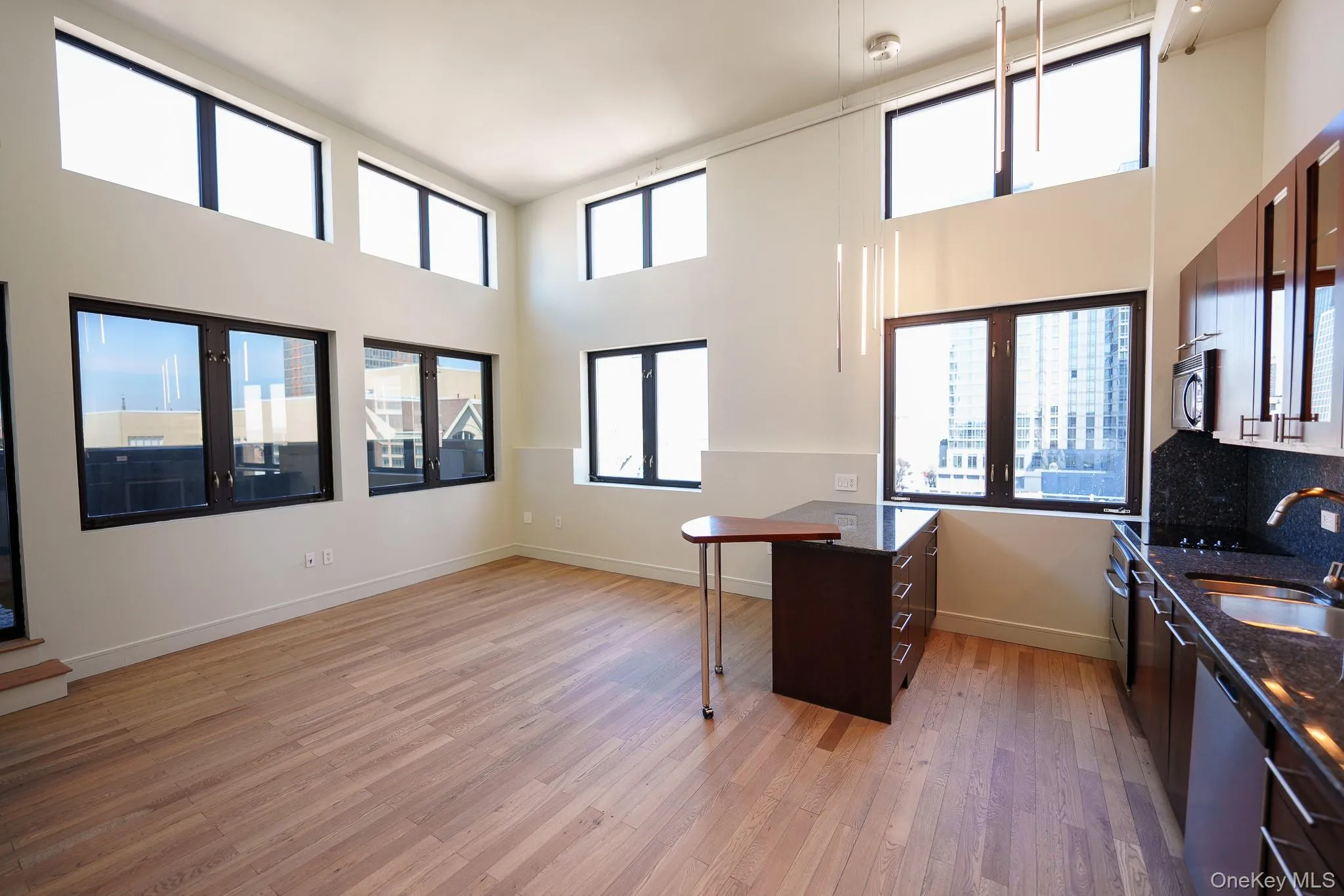 Kitchen with a breakfast bar, a high ceiling, dark stone countertops, stainless steel dishwasher, and a peninsula Kitchen with a breakfast bar, a high ceiling, dark stone countertops, stainless steel dishwasher, and a peninsula