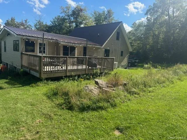 Rear view of property with a wooden deck, metal roof, and a lawn Rear view of property with a wooden deck, metal roof, and a lawn