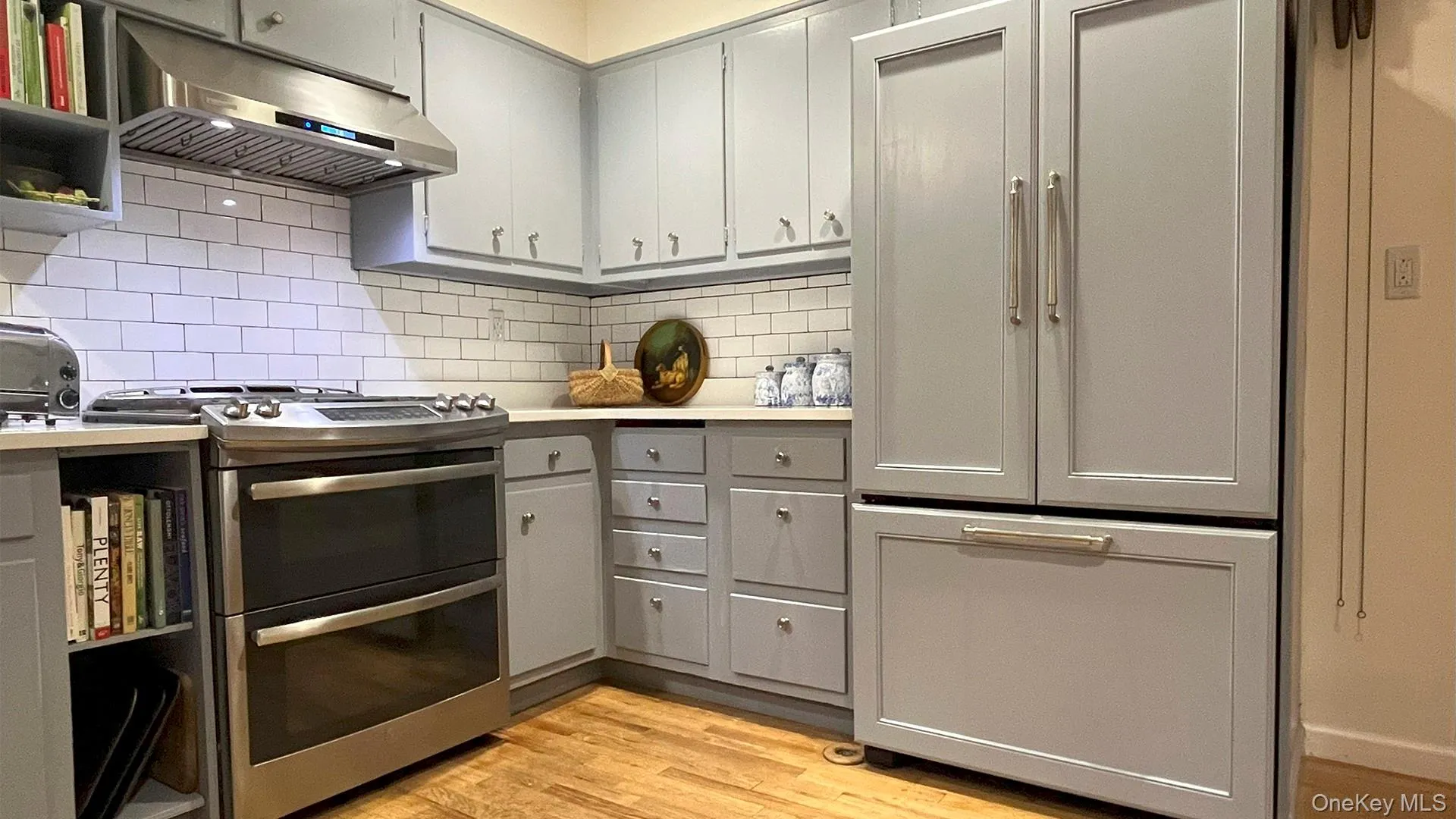 Kitchen featuring range with two ovens, under cabinet range hood, gray cabinetry, light countertops, and light wood-type flooring Kitchen featuring range with two ovens, under cabinet range hood, gray cabinetry, light countertops, and light wood-type flooring