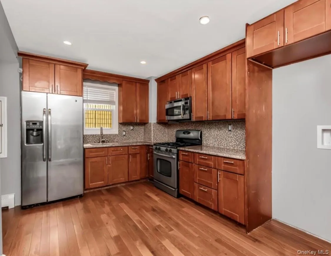 Kitchen featuring stainless steel appliances, wood finish cabinets, light wood-style floors, light stone counters, and recessed lighting with washer/dryer hookup Kitchen featuring stainless steel appliances, wood finish cabinets, light wood-style floors, light stone counters, and recessed lighting with washer/dryer hookup