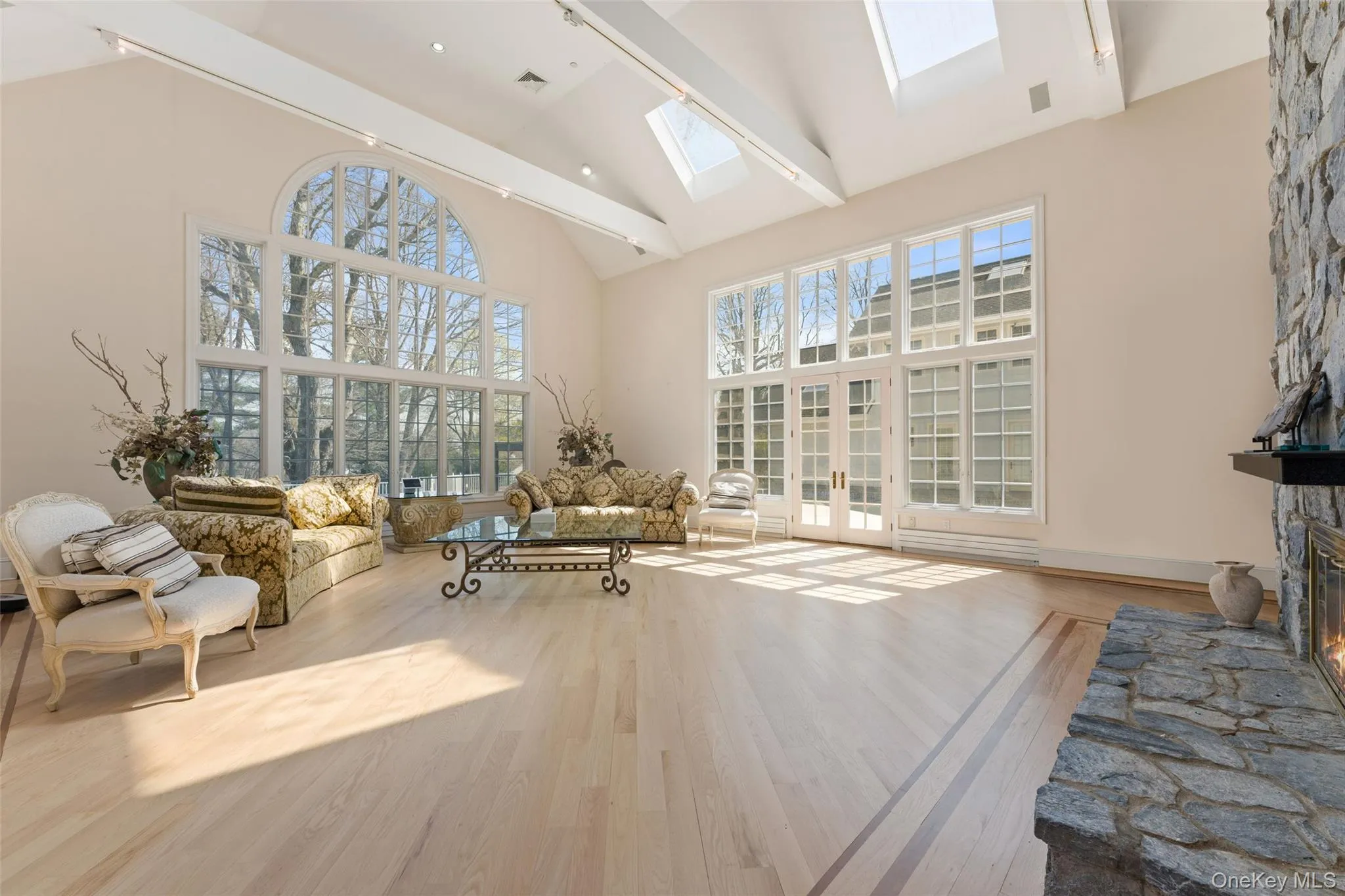 Living room with vaulted ceiling, light wood-type flooring, a stone fireplace, and a skylight Living room with vaulted ceiling, light wood-type flooring, a stone fireplace, and a skylight