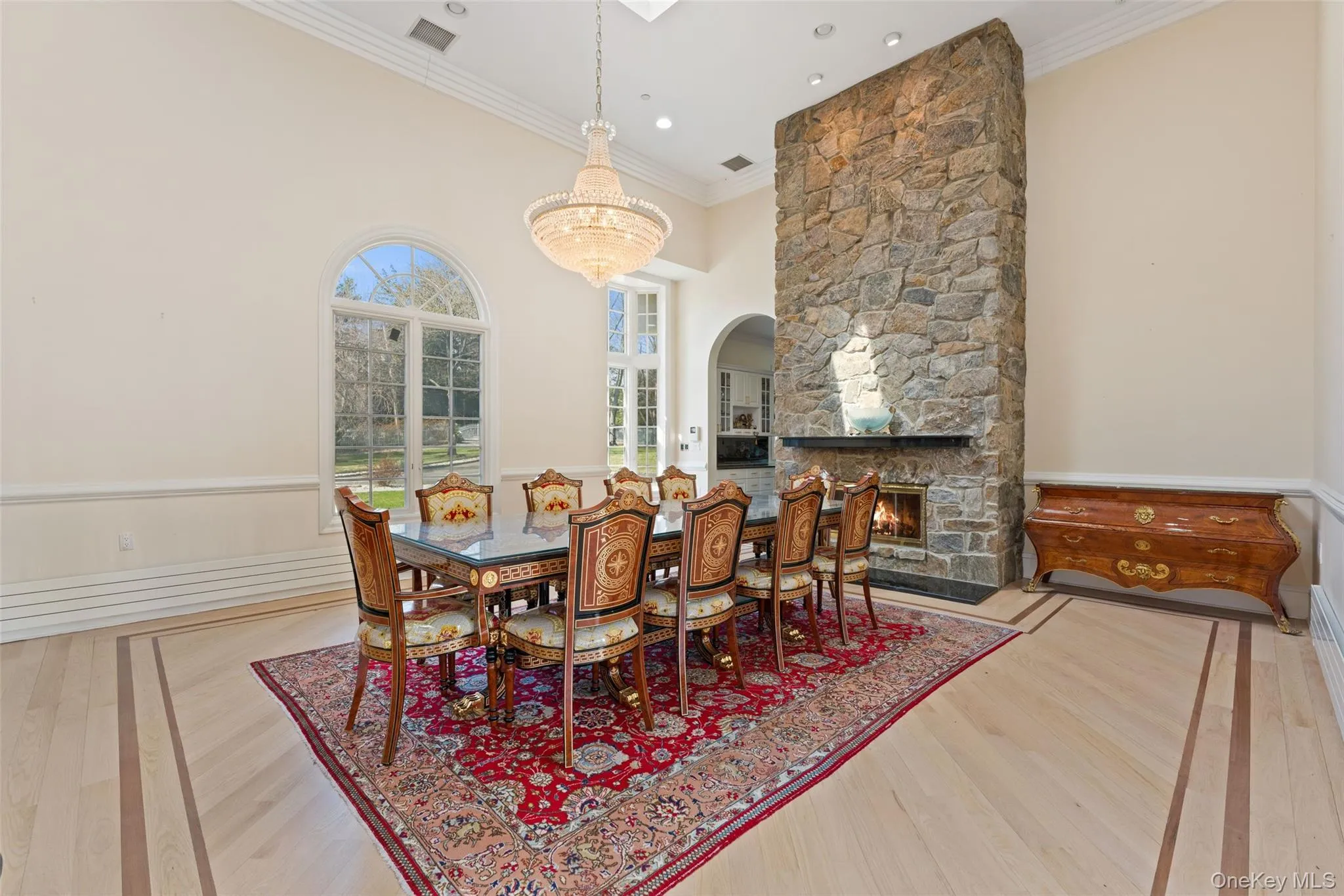Dining area featuring hardwood floors with an inlaid border, a stone fireplace, and arched windows Dining area featuring hardwood floors with an inlaid border, a stone fireplace, and arched windows