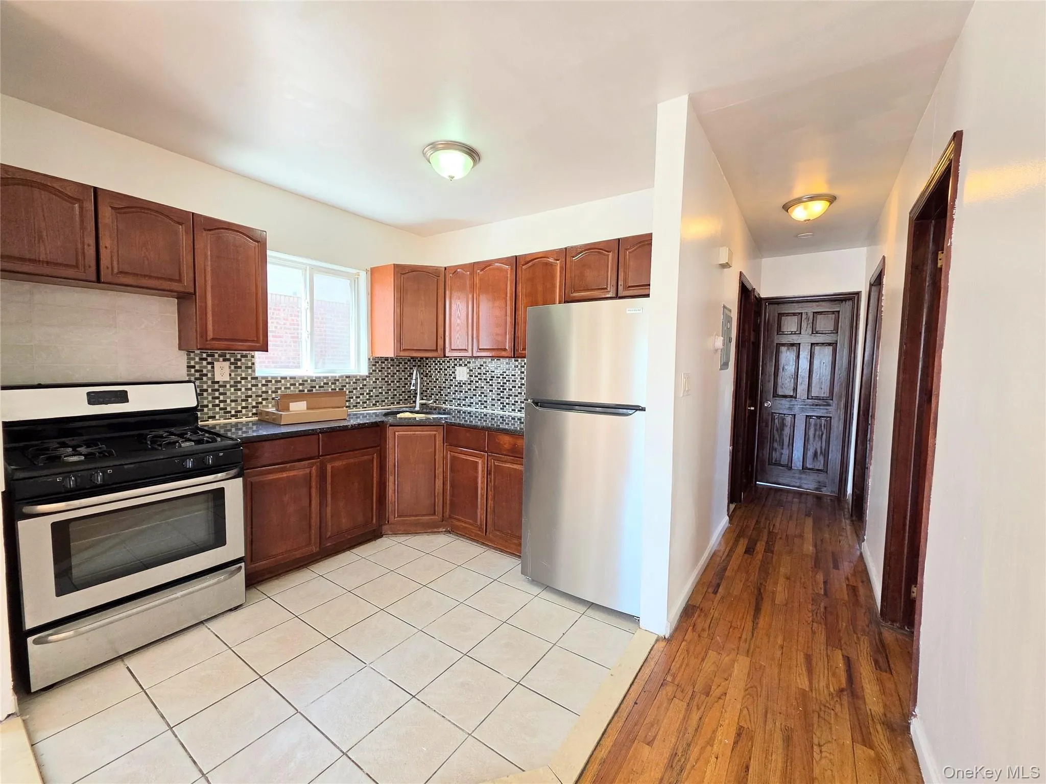 Kitchen featuring stainless steel appliances, gas stove, light wood finished floors, decorative backsplash, dark stone countertops, and wood cabinetry Kitchen featuring stainless steel appliances, gas stove, light wood finished floors, decorative backsplash, dark stone countertops, and wood cabinetry