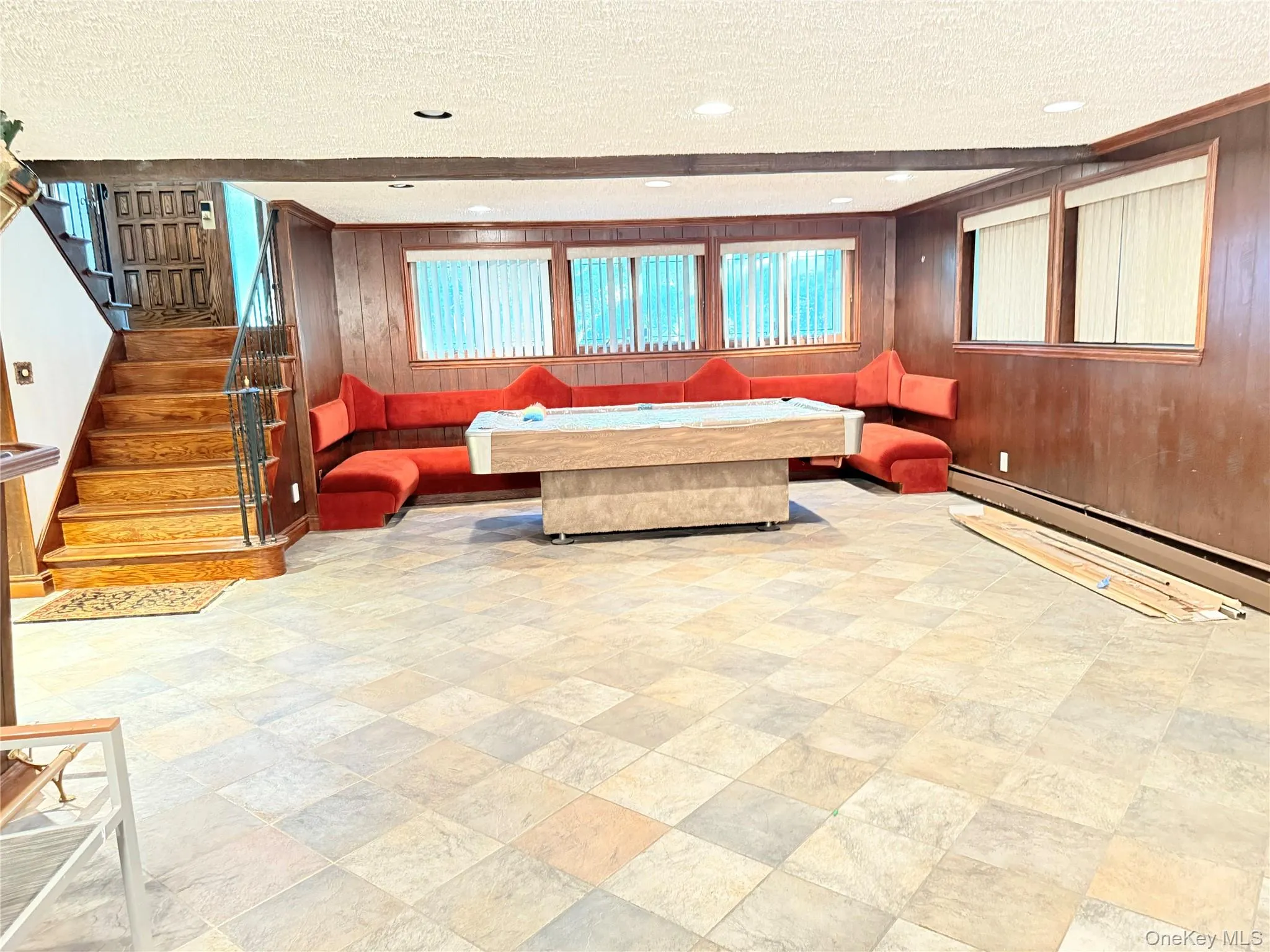 Spacious recreation room featuring tiled flooring, wood paneling, and an extensive built-in seating area Spacious recreation room featuring tiled flooring, wood paneling, and an extensive built-in seating area