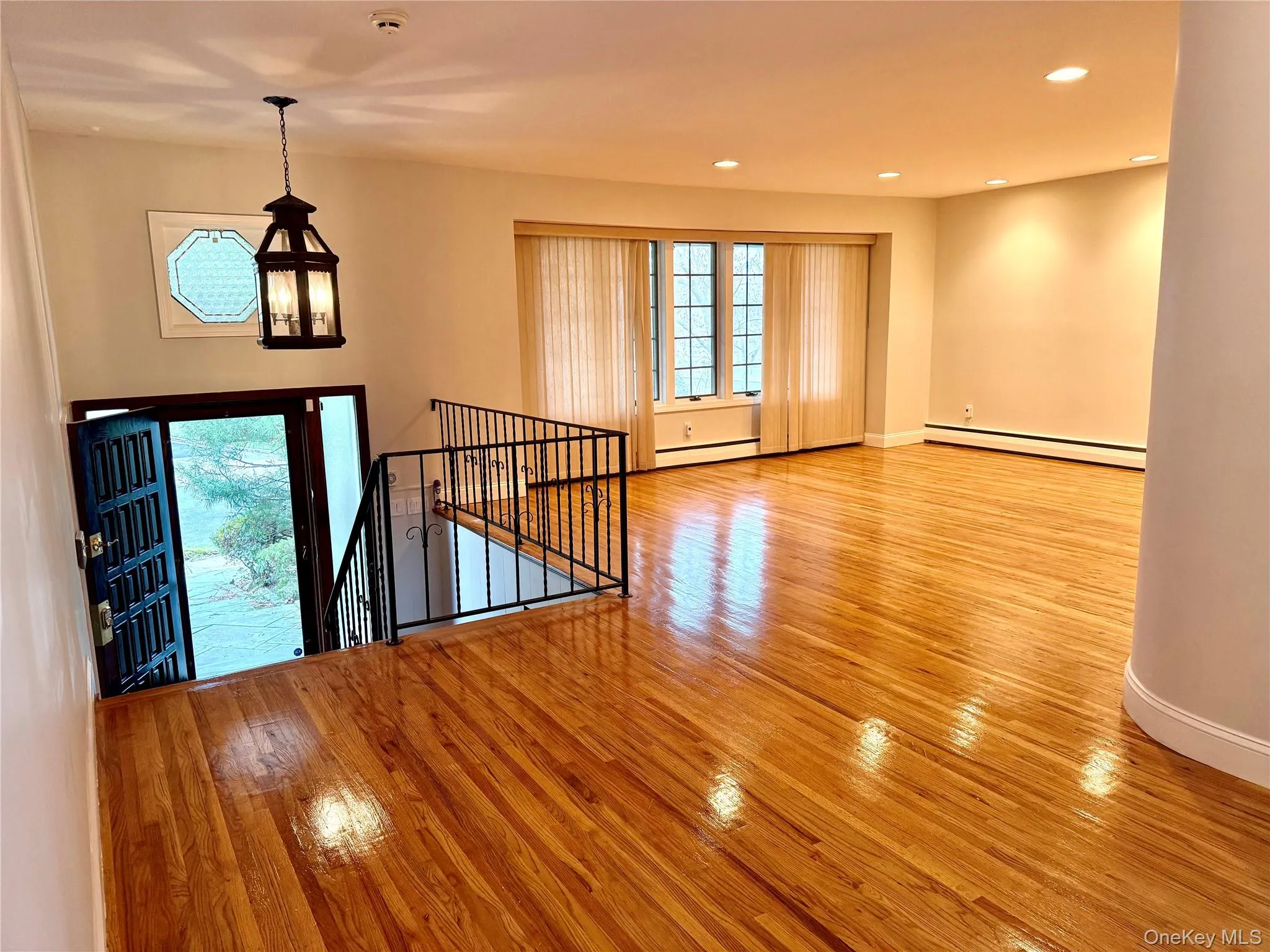 Entryway and living area featuring polished hardwood floors, a decorative iron railing, and recessed lighting Entryway and living area featuring polished hardwood floors, a decorative iron railing, and recessed lighting