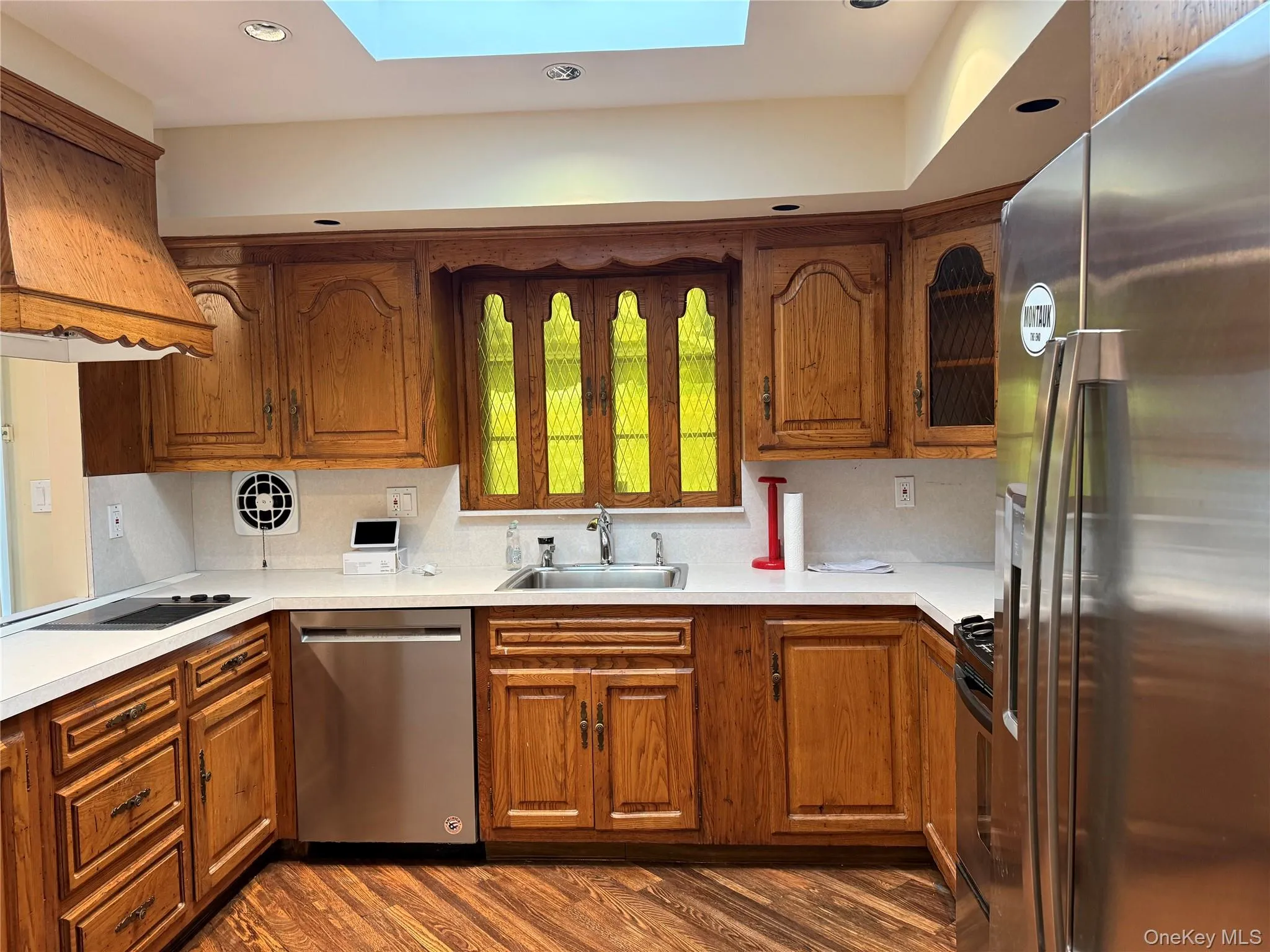 Kitchen featuring wood cabinetry, stainless steel appliances, white countertops, and a skylight Kitchen featuring wood cabinetry, stainless steel appliances, white countertops, and a skylight