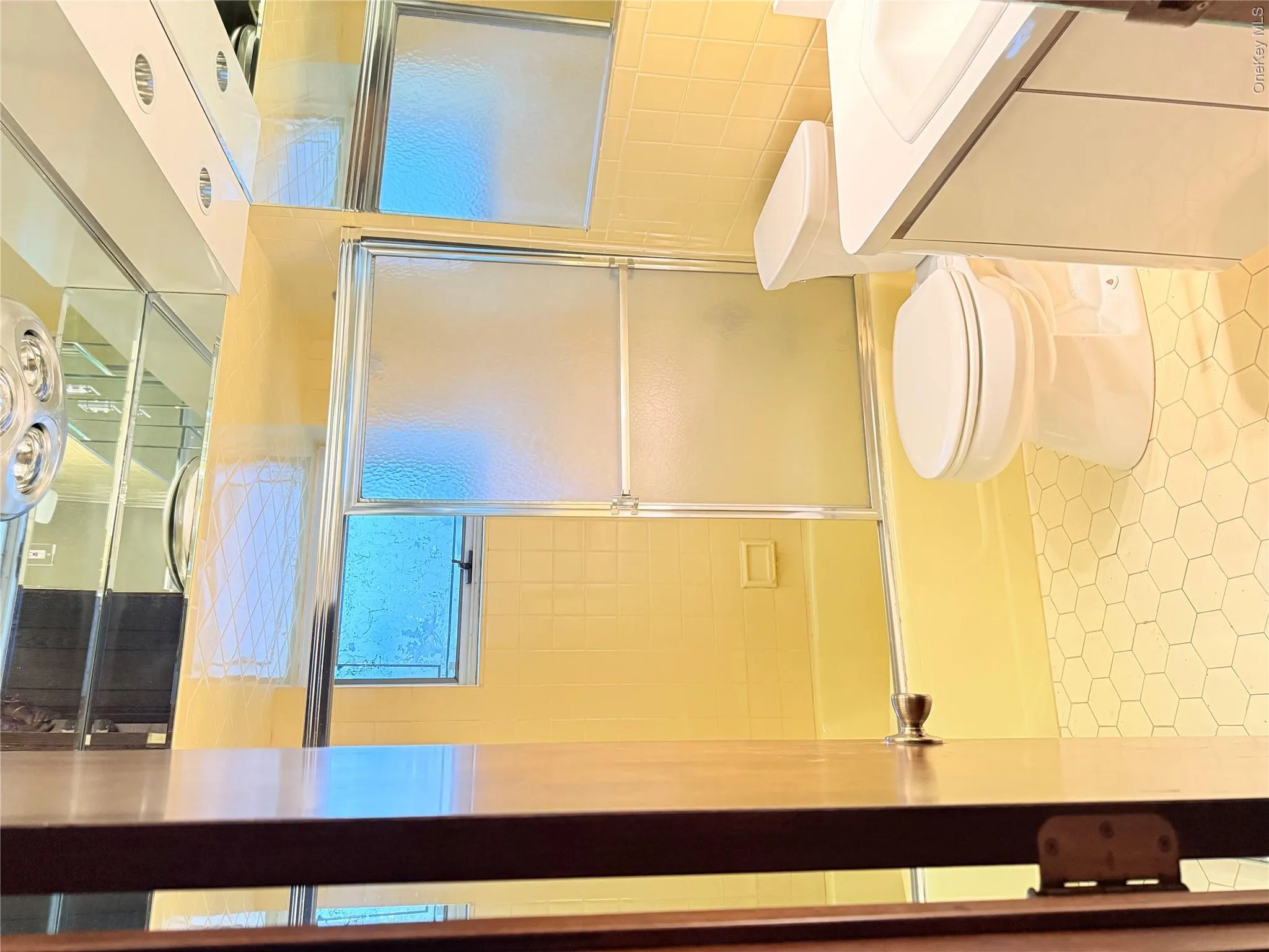 Bathroom featuring hexagonal floor tiles, a bathtub with a sliding glass door, and a white vanity with an integrated sink Bathroom featuring hexagonal floor tiles, a bathtub with a sliding glass door, and a white vanity with an integrated sink