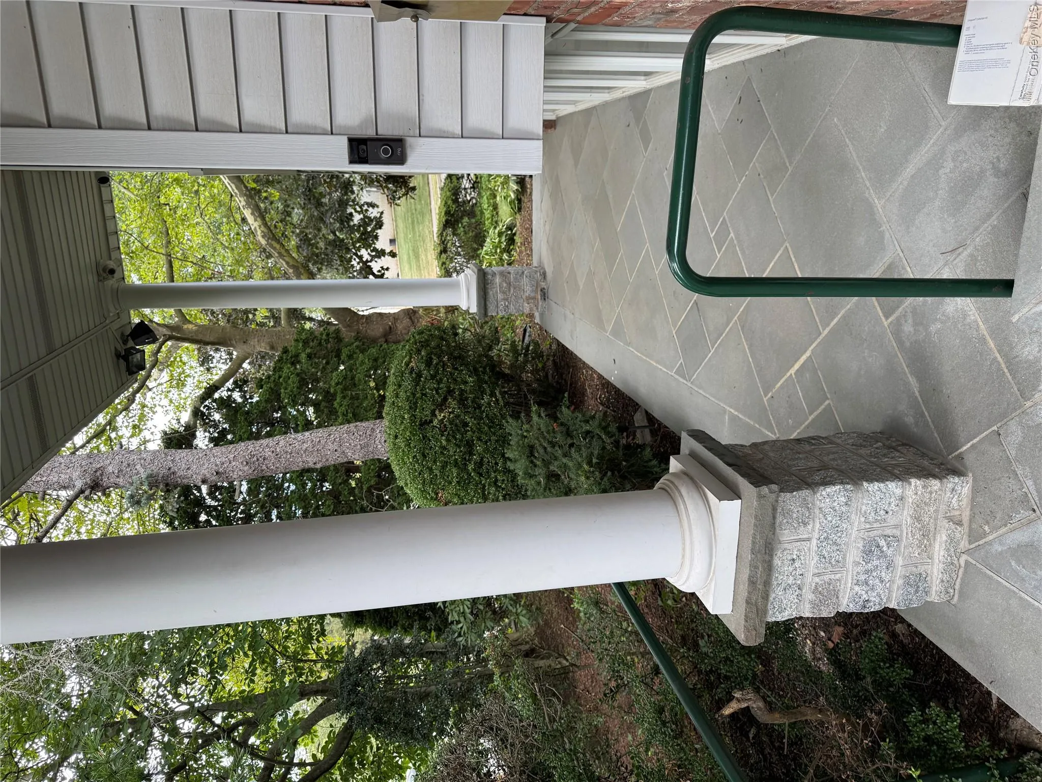 The property features a stone paver walkway and a columned porch, with a view of mature trees and landscaping The property features a stone paver walkway and a columned porch, with a view of mature trees and landscaping