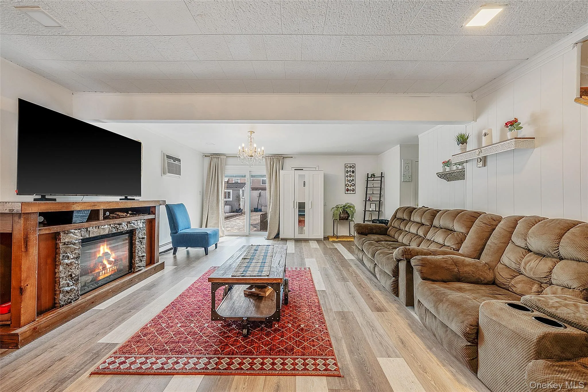Living room with a glass covered fireplace, light wood-style flooring, and suspended lighting Living room with a glass covered fireplace, light wood-style flooring, and suspended lighting