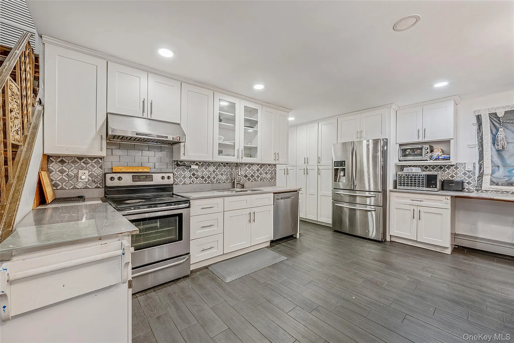 Kitchen with stainless steel appliances, glass fronted cabinets, white cabinets, dark wood-type flooring, and recessed lighting Kitchen with stainless steel appliances, glass fronted cabinets, white cabinets, dark wood-type flooring, and recessed lighting