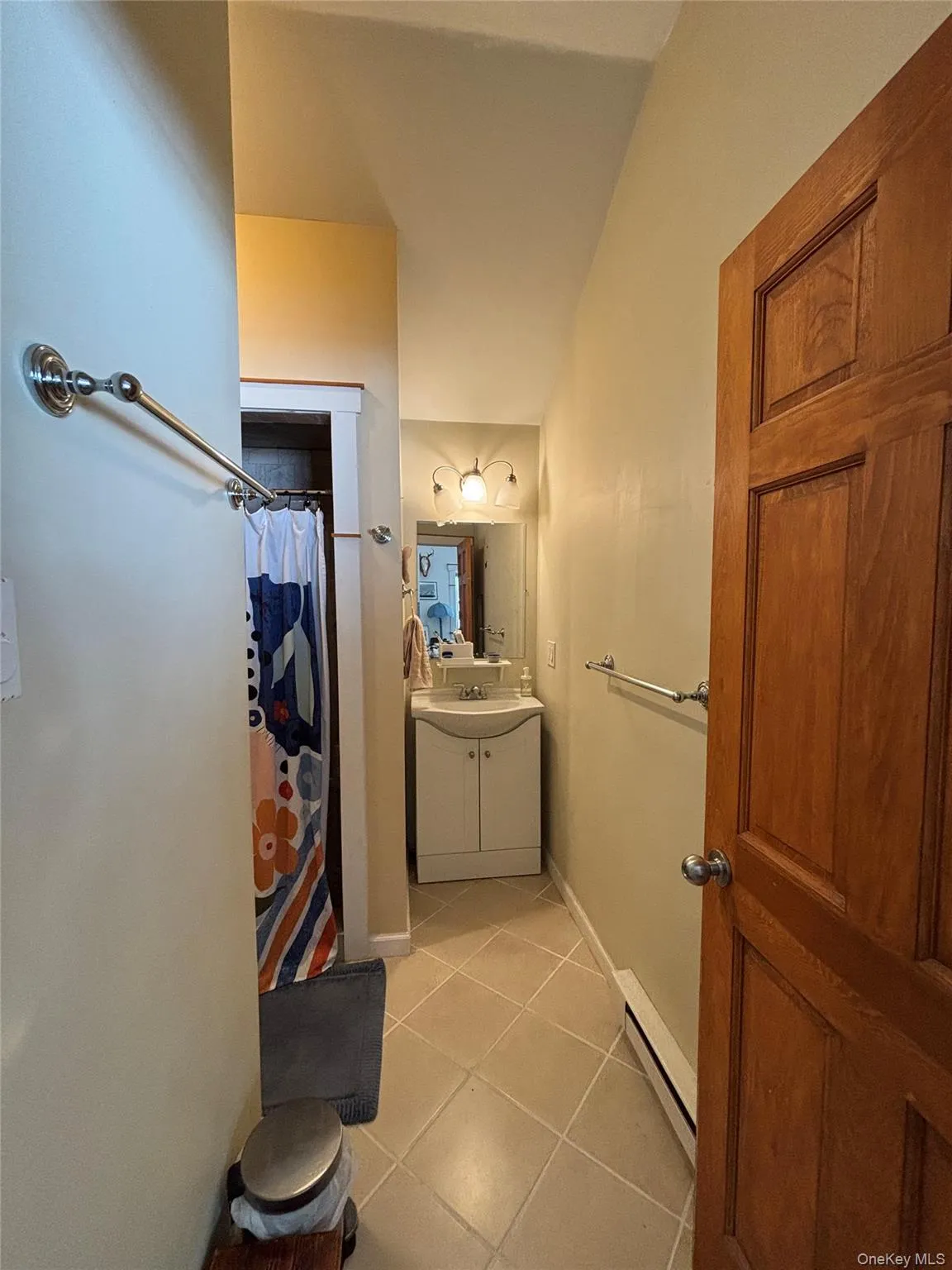 Full bathroom featuring vanity, a shower with shower curtain, light tile patterned flooring, and baseboard heating Full bathroom featuring vanity, a shower with shower curtain, light tile patterned flooring, and baseboard heating