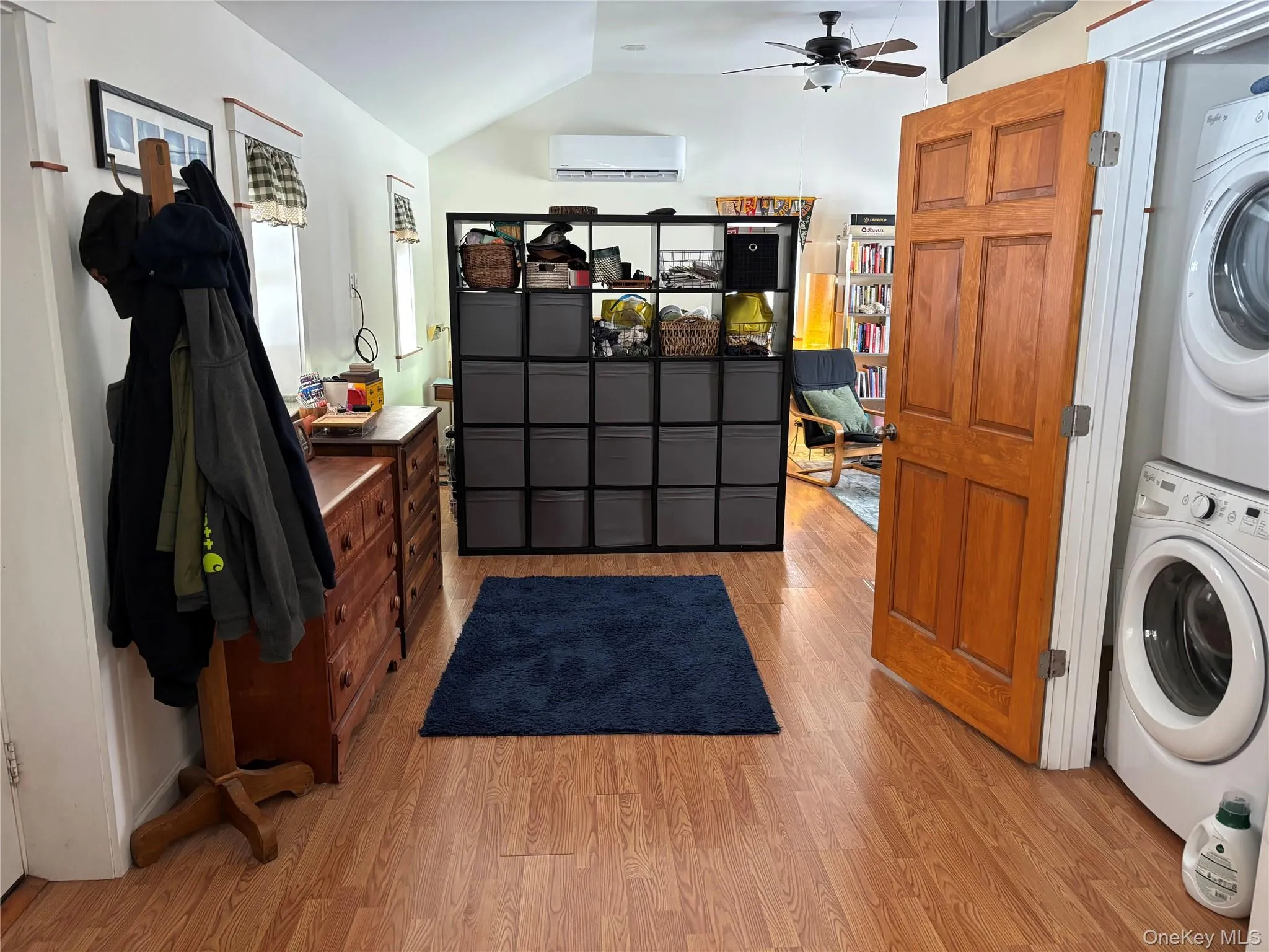 Laundry area featuring light wood-style flooring, stacked washer and clothes dryer, lofted ceiling, and a ceiling fan Laundry area featuring light wood-style flooring, stacked washer and clothes dryer, lofted ceiling, and a ceiling fan