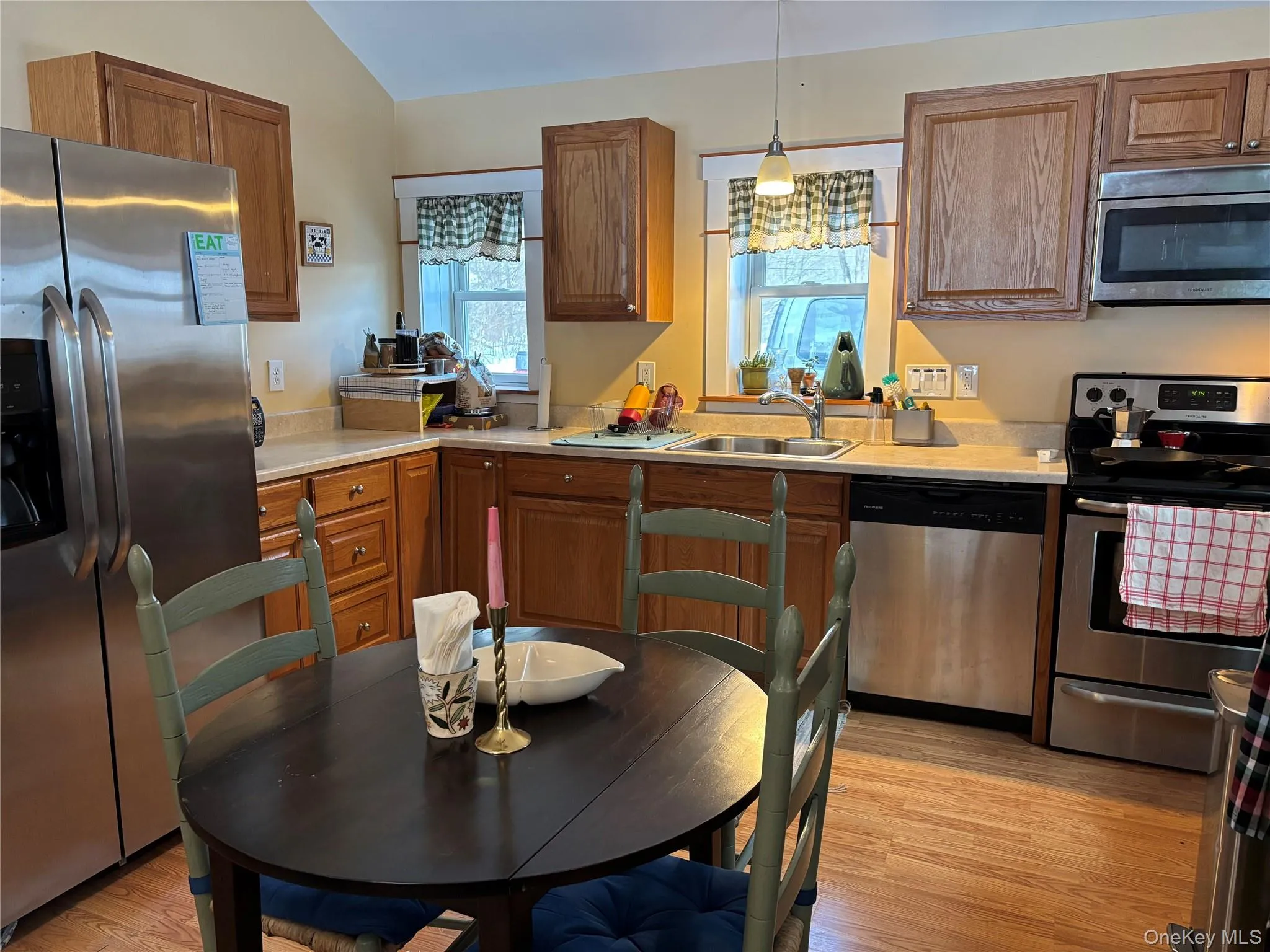 Kitchen featuring stainless steel appliances, light countertops, light wood-type flooring, wood finish cabinets, and vaulted ceiling Kitchen featuring stainless steel appliances, light countertops, light wood-type flooring, wood finish cabinets, and vaulted ceiling
