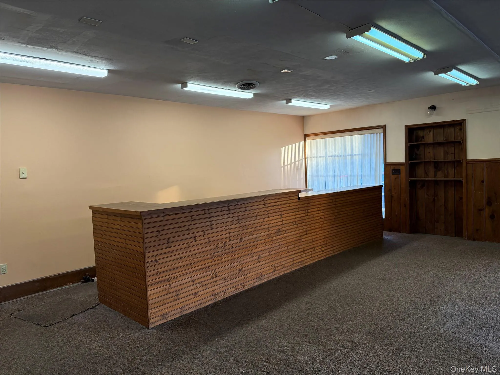 Unfurnished Retail with desk featuring wood walls, dark carpet, and a wainscoted wall Unfurnished Retail with desk featuring wood walls, dark carpet, and a wainscoted wall