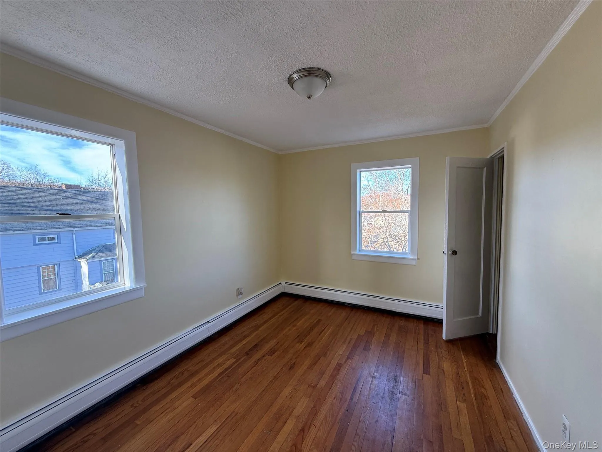 Unfurnished room with ornamental molding, a textured ceiling, a baseboard radiator, baseboard heating, and dark wood-style flooring Unfurnished room with ornamental molding, a textured ceiling, a baseboard radiator, baseboard heating, and dark wood-style flooring