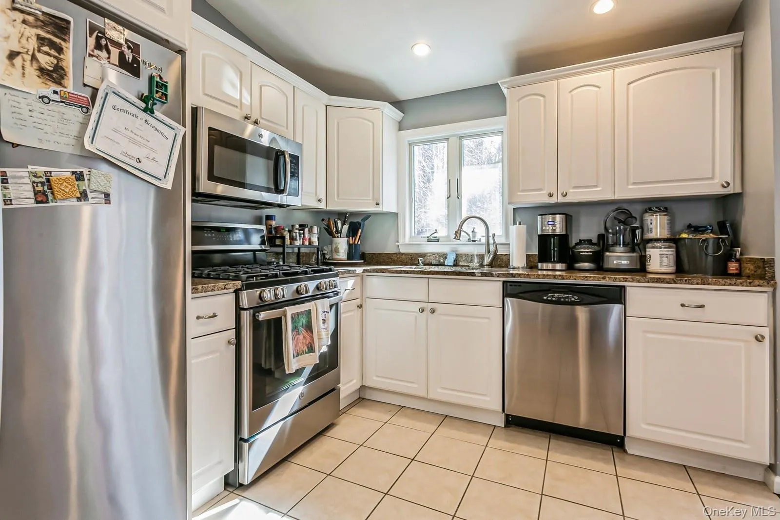 Kitchen with appliances with stainless steel finishes, light tile patterned flooring, dark stone countertops, and white cabinetry Kitchen with appliances with stainless steel finishes, light tile patterned flooring, dark stone countertops, and white cabinetry