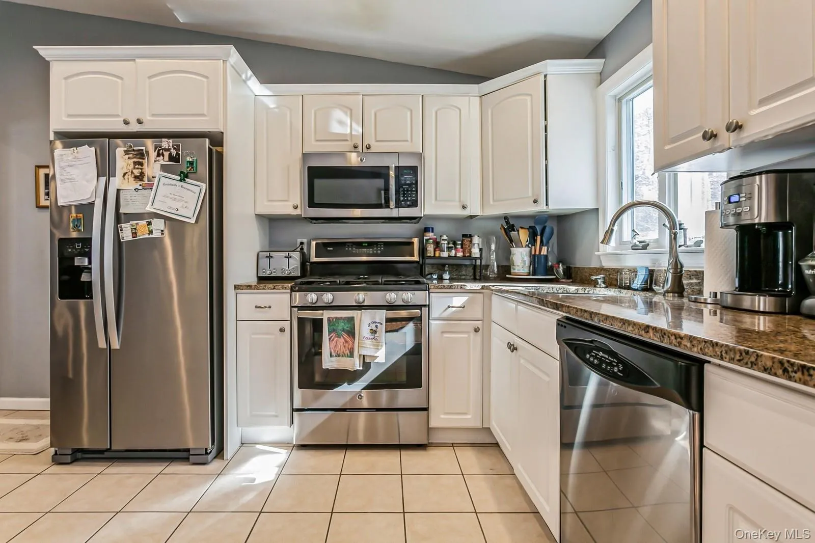 Kitchen featuring light tile patterned floors, lofted ceiling, stainless steel appliances, white cabinetry, and a sink Kitchen featuring light tile patterned floors, lofted ceiling, stainless steel appliances, white cabinetry, and a sink