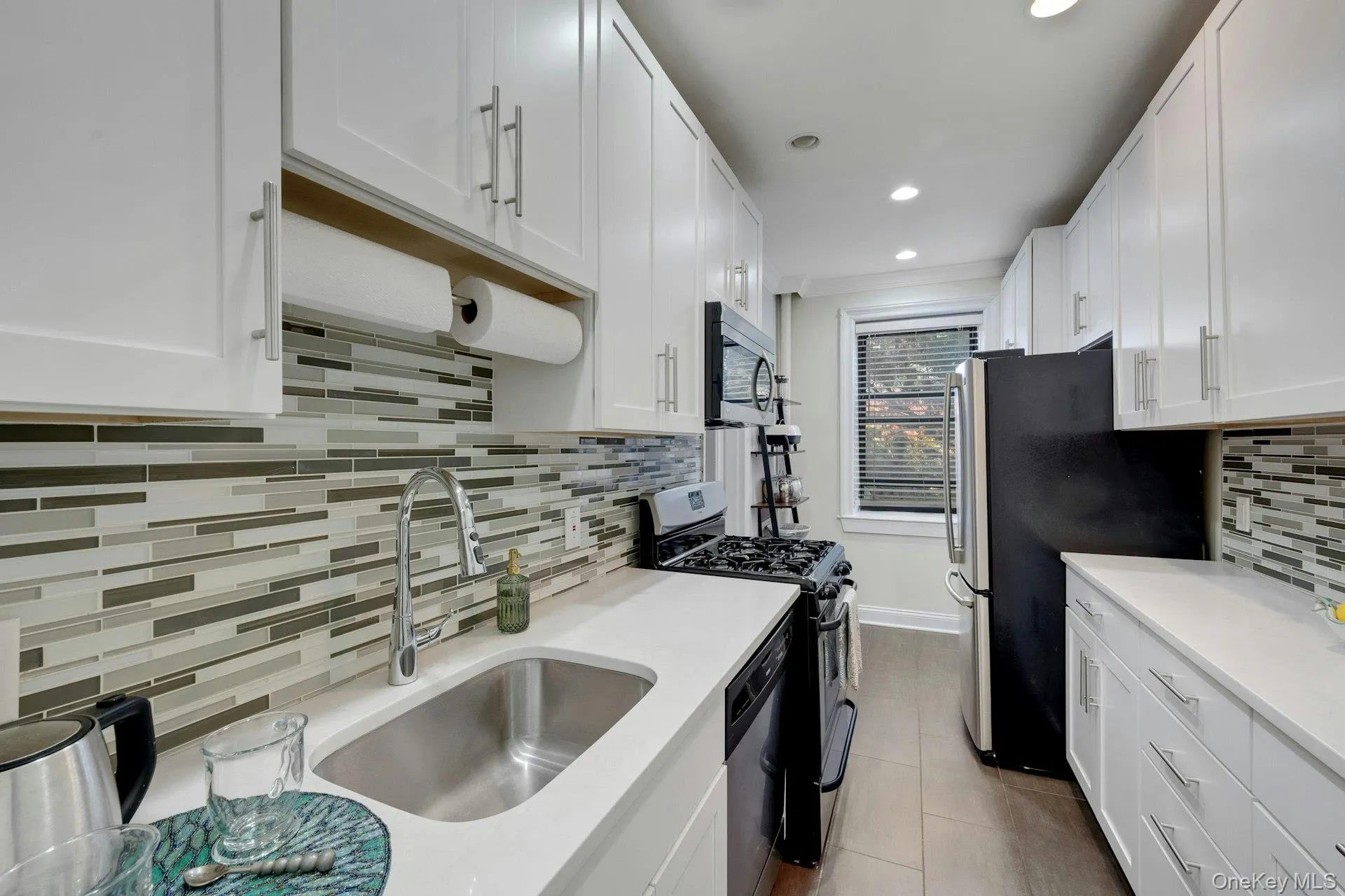 Kitchen with backsplash, white cabinetry, appliances with stainless steel finishes, recessed lighting, and light tile flooring Kitchen with backsplash, white cabinetry, appliances with stainless steel finishes, recessed lighting, and light tile flooring