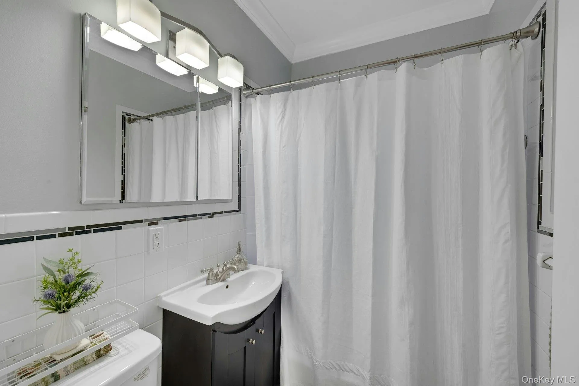 Bathroom featuring vanity, curtained shower, crown molding, tile walls, and tasteful backsplash Bathroom featuring vanity, curtained shower, crown molding, tile walls, and tasteful backsplash