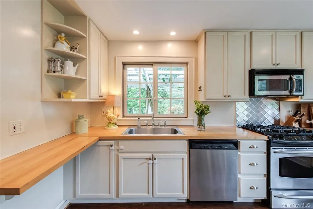 Kitchen with wooden counters, stainless steel appliances, white cabinets, sink, and backsplash Kitchen with wooden counters, stainless steel appliances, white cabinets, sink, and backsplash