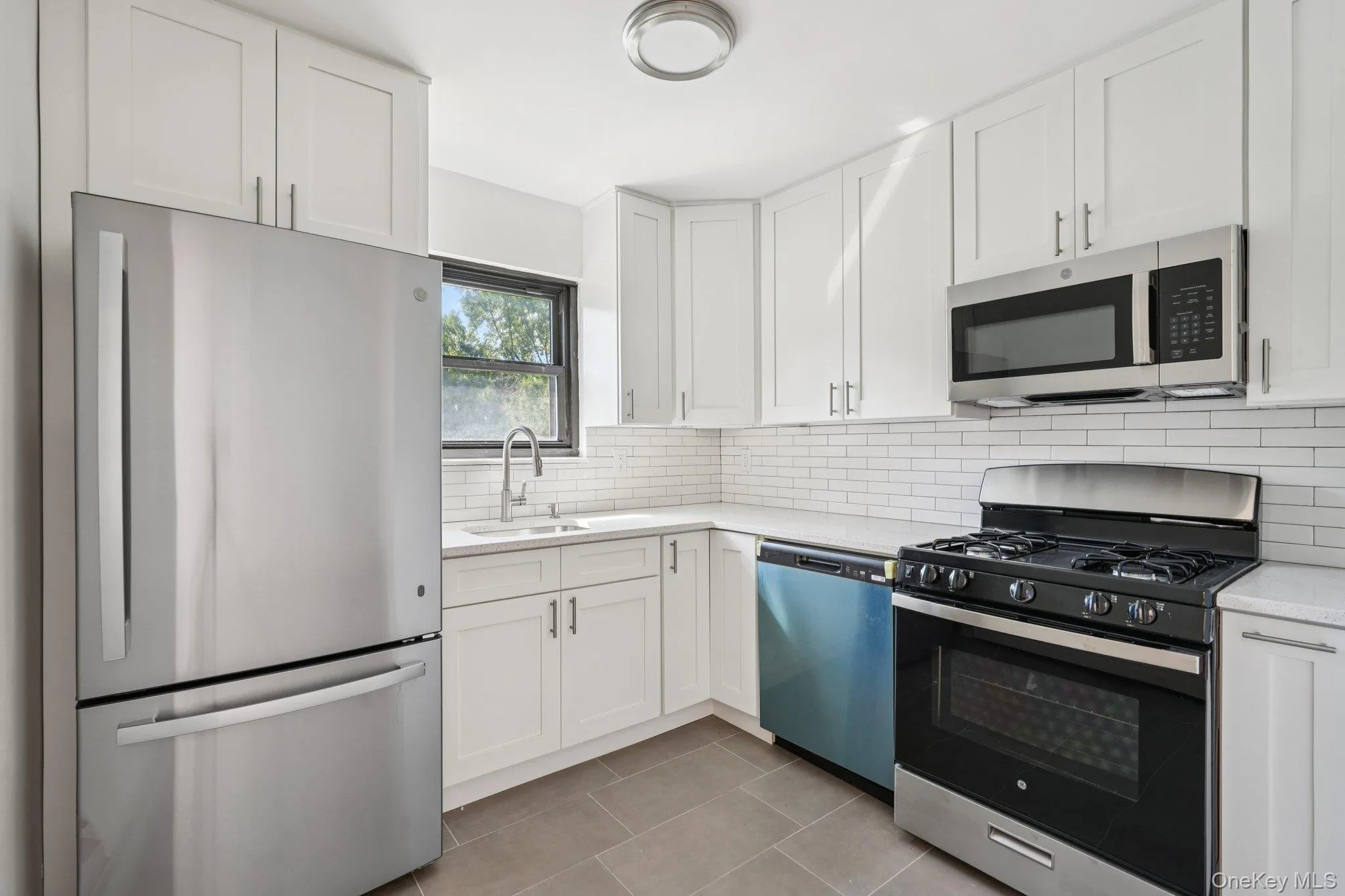 Kitchen with stainless steel appliances, white cabinets, tasteful backsplash, and light stone countertops Kitchen with stainless steel appliances, white cabinets, tasteful backsplash, and light stone countertops