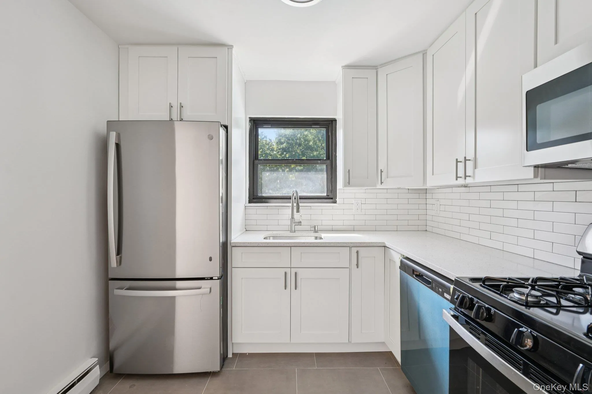 Kitchen featuring appliances with stainless steel finishes, white cabinets, tasteful backsplash, light tile patterned floors, and a baseboard radiator Kitchen featuring appliances with stainless steel finishes, white cabinets, tasteful backsplash, light tile patterned floors, and a baseboard radiator