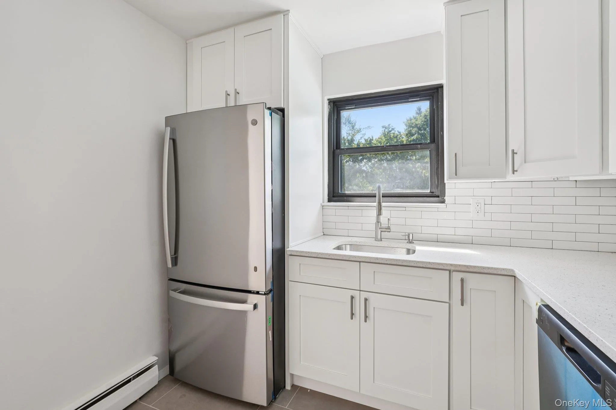 Kitchen featuring stainless steel appliances, a baseboard radiator, backsplash, white cabinetry, and light stone counters Kitchen featuring stainless steel appliances, a baseboard radiator, backsplash, white cabinetry, and light stone counters