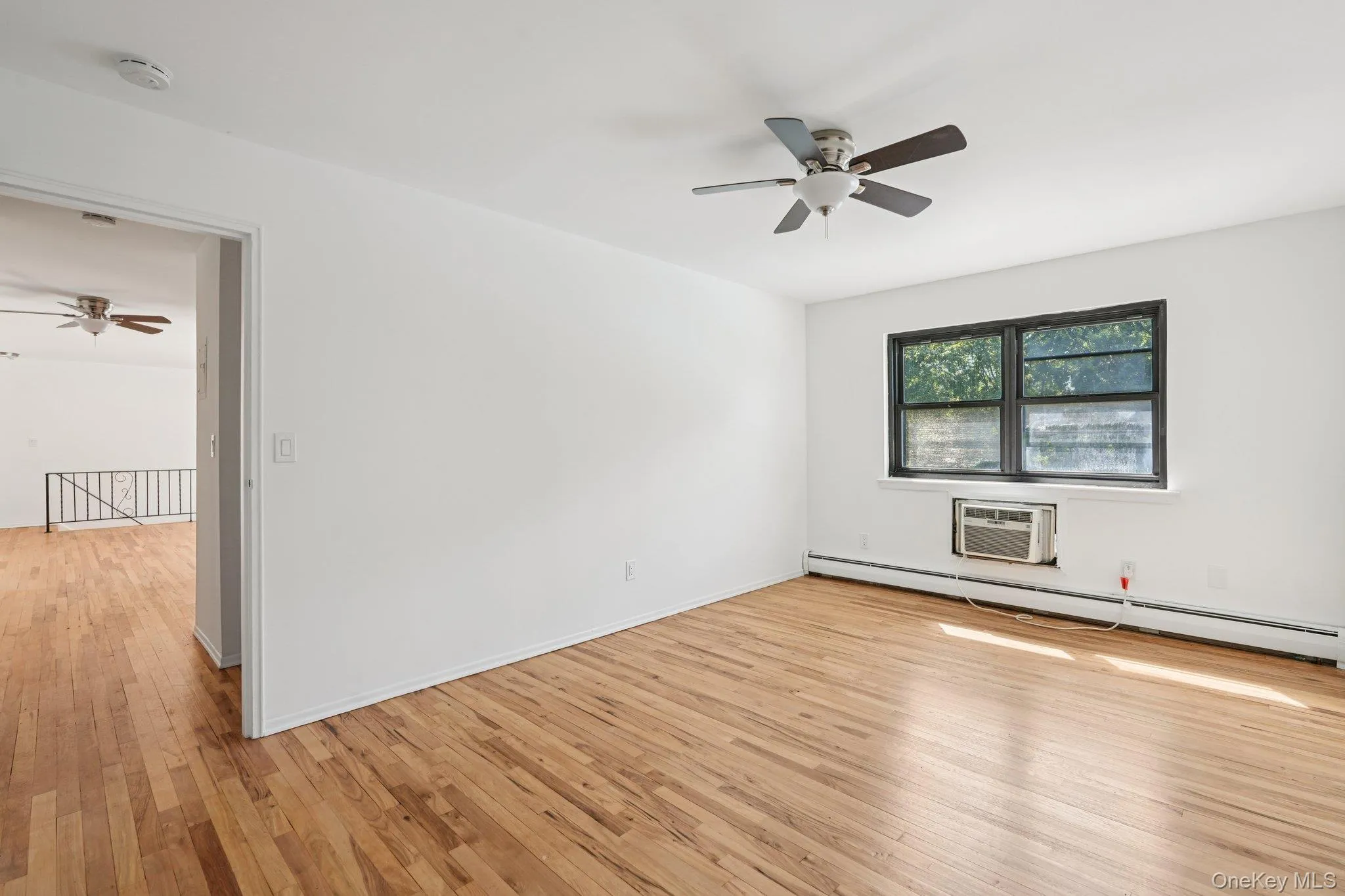 Spare room with a ceiling fan, light wood-style flooring, a baseboard radiator, and an AC wall unit Spare room with a ceiling fan, light wood-style flooring, a baseboard radiator, and an AC wall unit