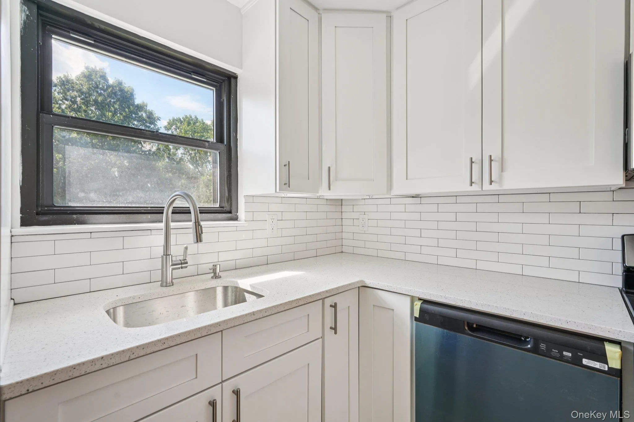 Kitchen featuring light stone counters, white cabinets, dishwasher, and tasteful backsplash Kitchen featuring light stone counters, white cabinets, dishwasher, and tasteful backsplash