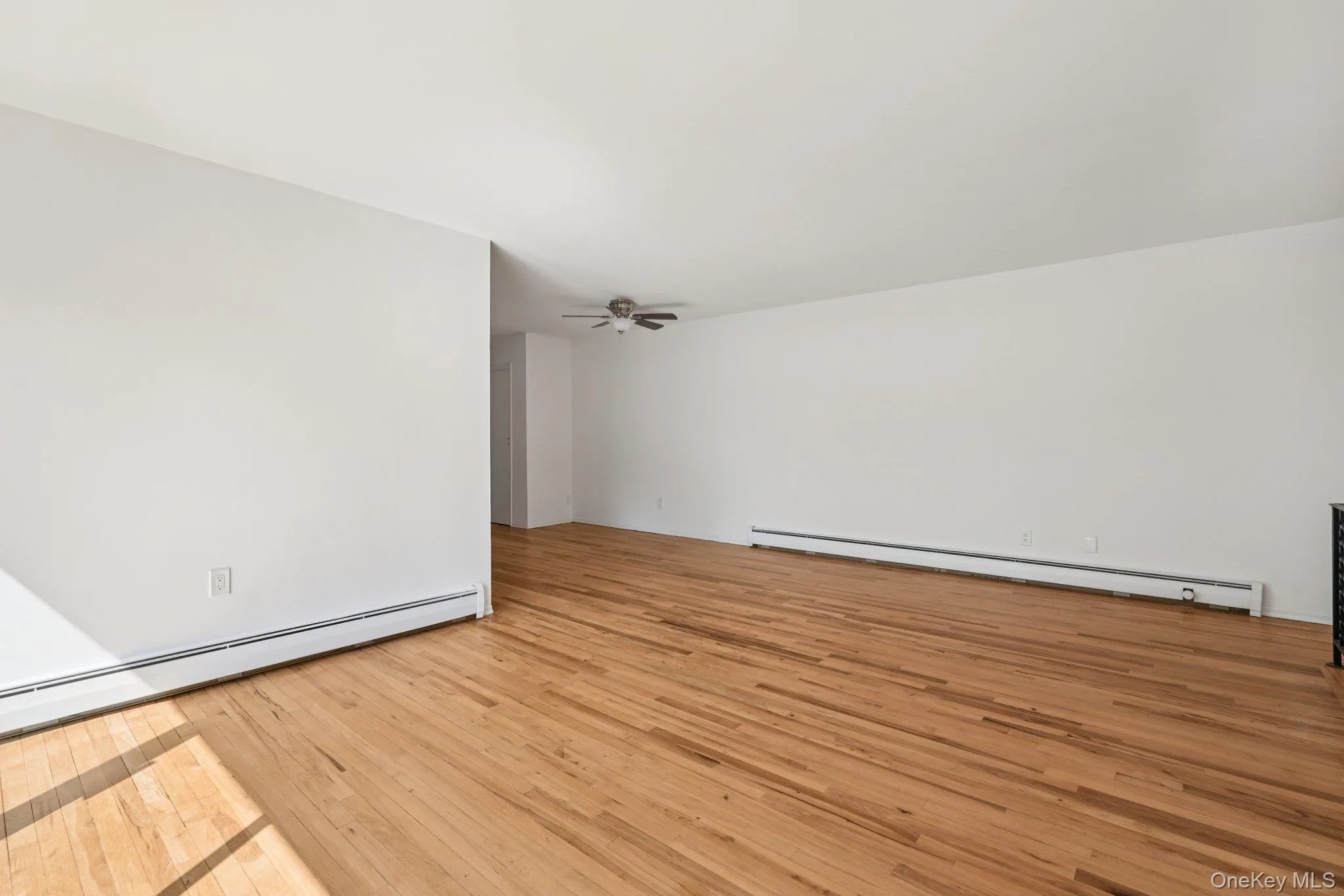 Spare room featuring light wood-style floors, a baseboard radiator, and ceiling fan Spare room featuring light wood-style floors, a baseboard radiator, and ceiling fan