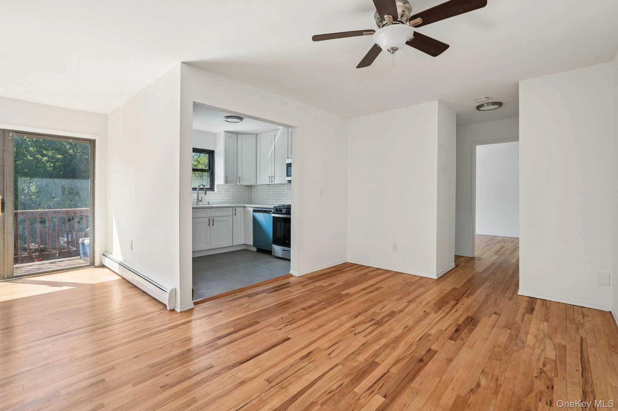 Unfurnished living room with baseboard heating, light wood-style floors, and a ceiling fan Unfurnished living room with baseboard heating, light wood-style floors, and a ceiling fan