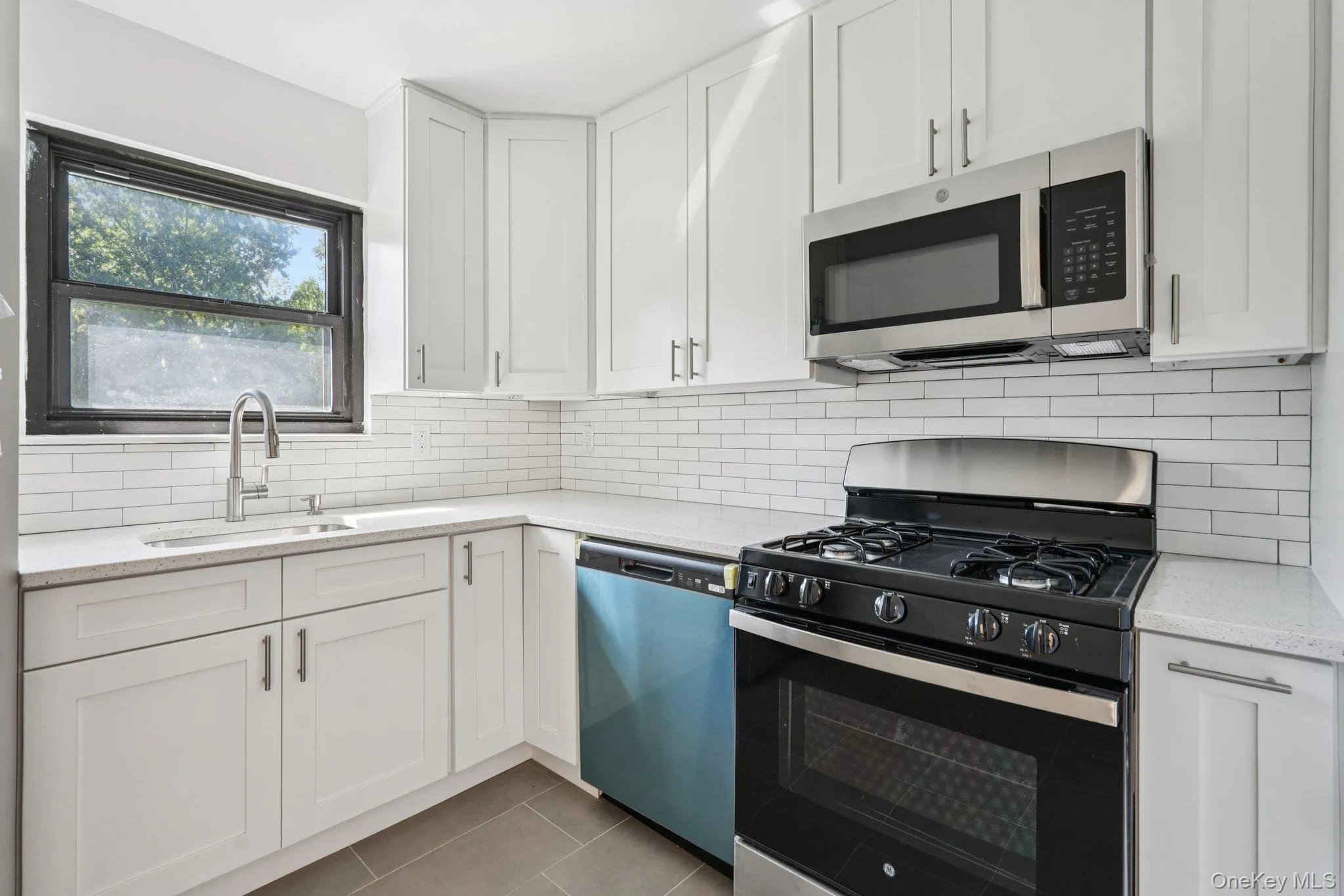 Kitchen featuring black gas range oven, stainless steel microwave, light stone counters, white cabinetry, and decorative backsplash Kitchen featuring black gas range oven, stainless steel microwave, light stone counters, white cabinetry, and decorative backsplash