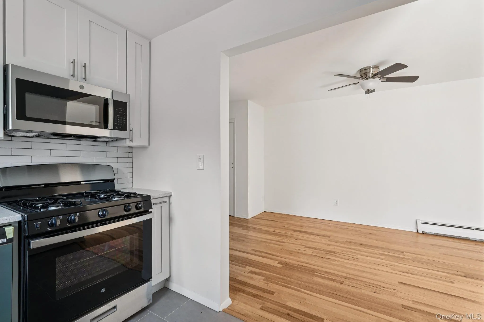 Kitchen featuring appliances with stainless steel finishes, decorative backsplash, white cabinetry, a ceiling fan, and light stone counters Kitchen featuring appliances with stainless steel finishes, decorative backsplash, white cabinetry, a ceiling fan, and light stone counters