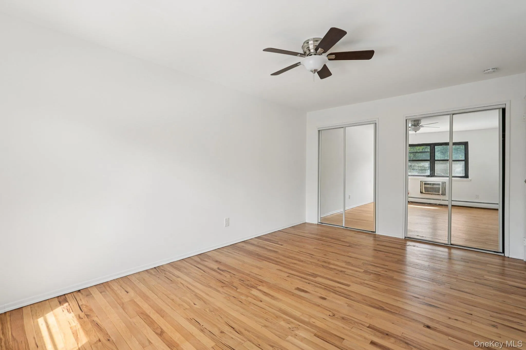 Unfurnished bedroom featuring multiple closets, light wood-style flooring, ceiling fan, and a baseboard heating unit Unfurnished bedroom featuring multiple closets, light wood-style flooring, ceiling fan, and a baseboard heating unit