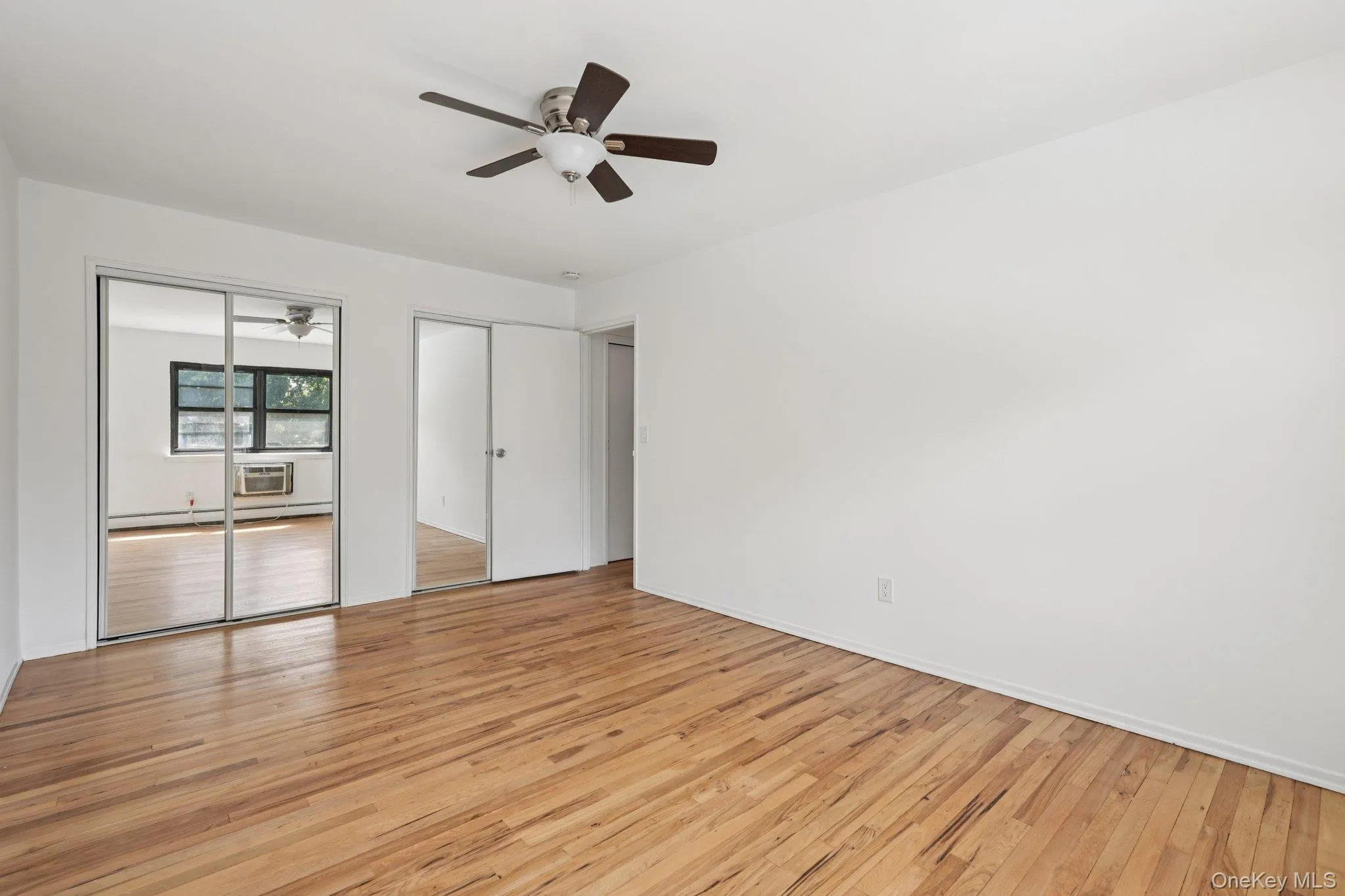 Unfurnished bedroom with light wood-type flooring, a ceiling fan, two closets, and a baseboard radiator Unfurnished bedroom with light wood-type flooring, a ceiling fan, two closets, and a baseboard radiator