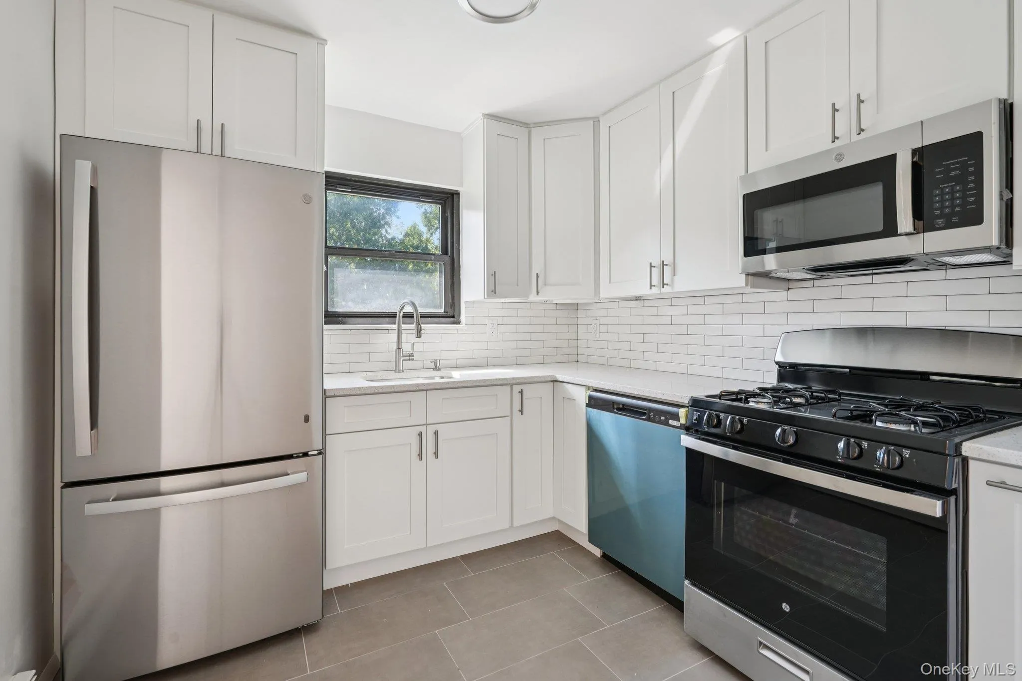 Kitchen with appliances with stainless steel finishes, white cabinetry, tasteful backsplash, and light stone countertops Kitchen with appliances with stainless steel finishes, white cabinetry, tasteful backsplash, and light stone countertops