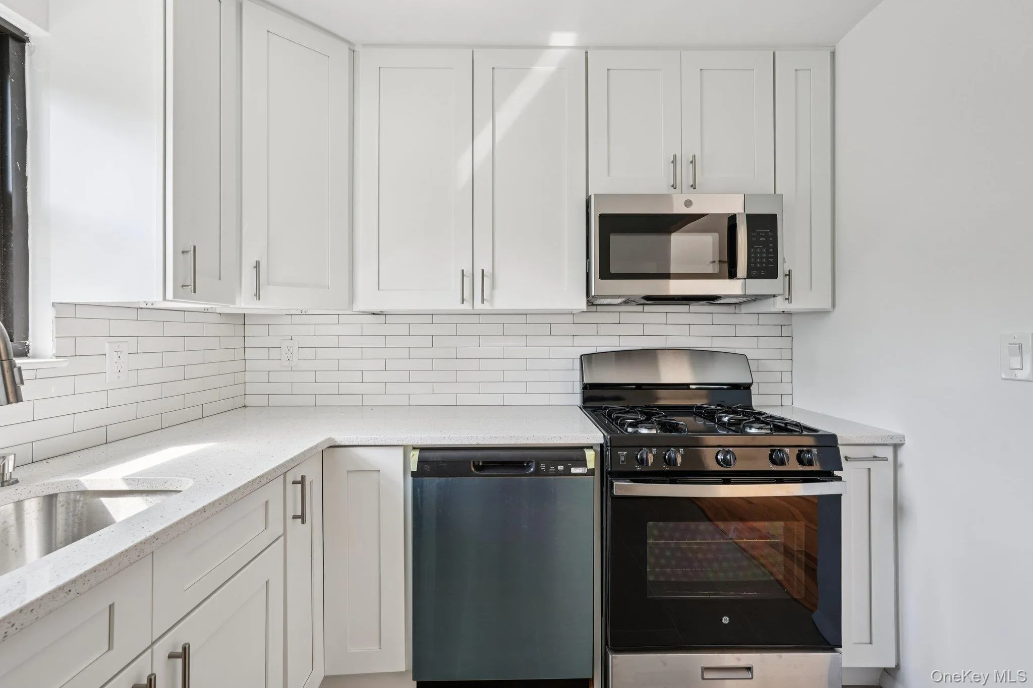 Kitchen featuring appliances with stainless steel finishes, white cabinetry, light stone countertops, and backsplash Kitchen featuring appliances with stainless steel finishes, white cabinetry, light stone countertops, and backsplash