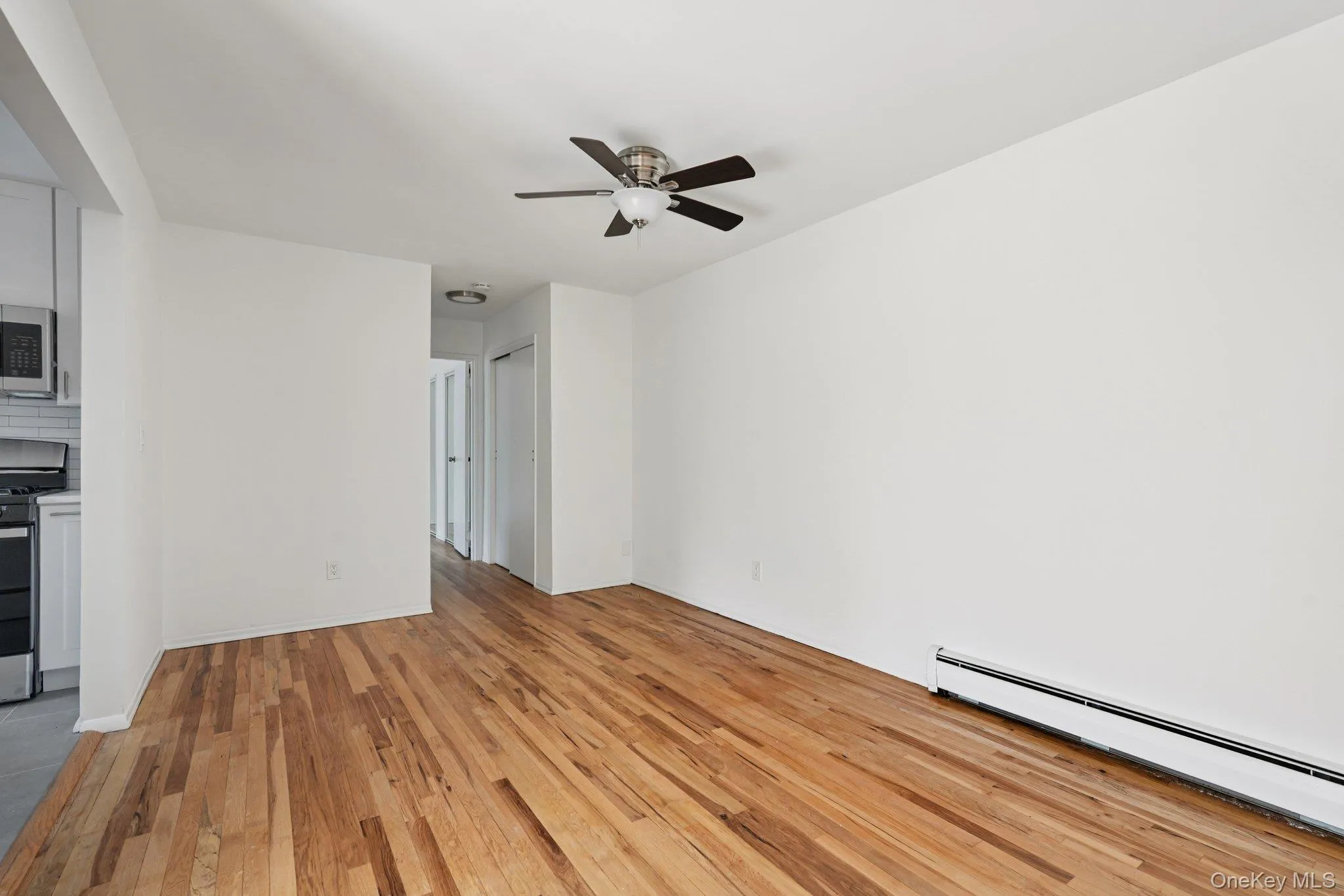 Unfurnished living room with baseboard heating, light wood-type flooring, and ceiling fan Unfurnished living room with baseboard heating, light wood-type flooring, and ceiling fan
