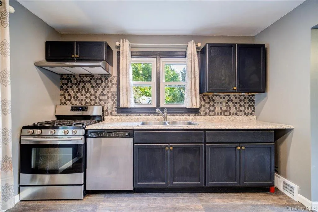 Kitchen with sink, light hardwood / wood-style flooring, exhaust hood, stainless steel appliances, and decorative backsplash Kitchen with sink, light hardwood / wood-style flooring, exhaust hood, stainless steel appliances, and decorative backsplash