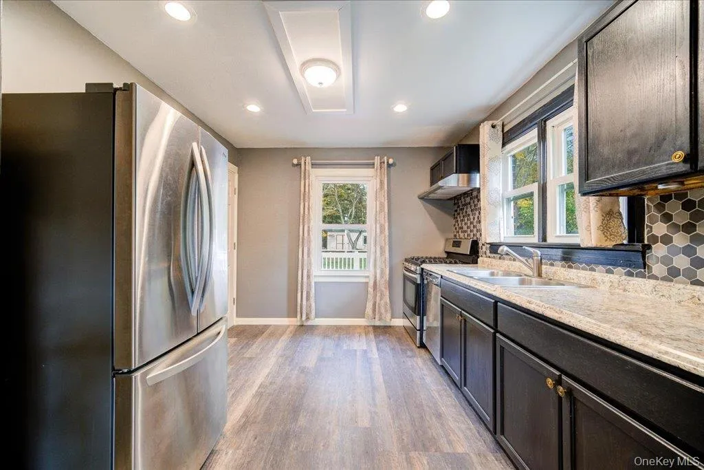 Kitchen featuring appliances with stainless steel finishes, decorative backsplash, light hardwood / wood-style flooring, dark brown cabinetry, and sink Kitchen featuring appliances with stainless steel finishes, decorative backsplash, light hardwood / wood-style flooring, dark brown cabinetry, and sink