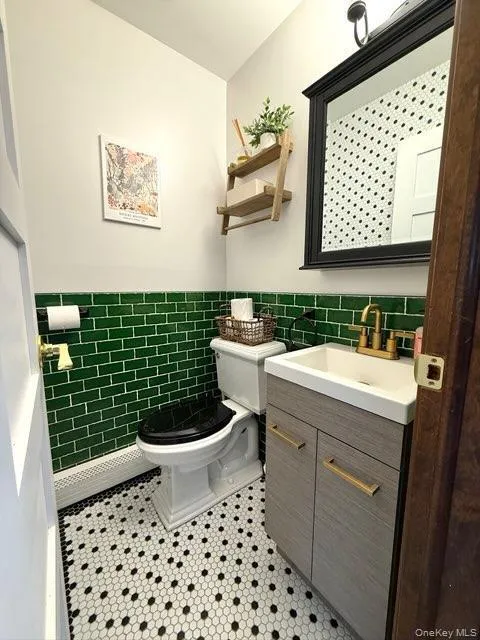 Half bath featuring a wainscoted wall, toilet, vanity, tile patterned flooring, and tile walls Half bath featuring a wainscoted wall, toilet, vanity, tile patterned flooring, and tile walls
