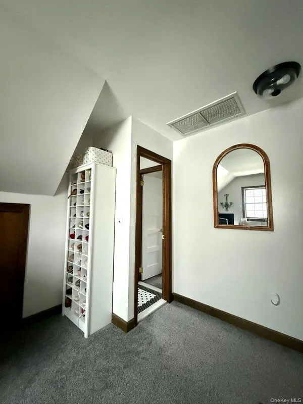 Additional living space featuring baseboards, dark colored carpet, lofted ceiling, and visible vents Additional living space featuring baseboards, dark colored carpet, lofted ceiling, and visible vents