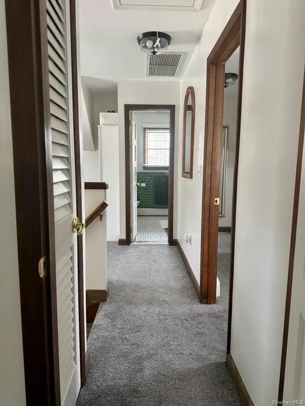 Corridor featuring carpet flooring, baseboards, attic access, and visible vents Corridor featuring carpet flooring, baseboards, attic access, and visible vents