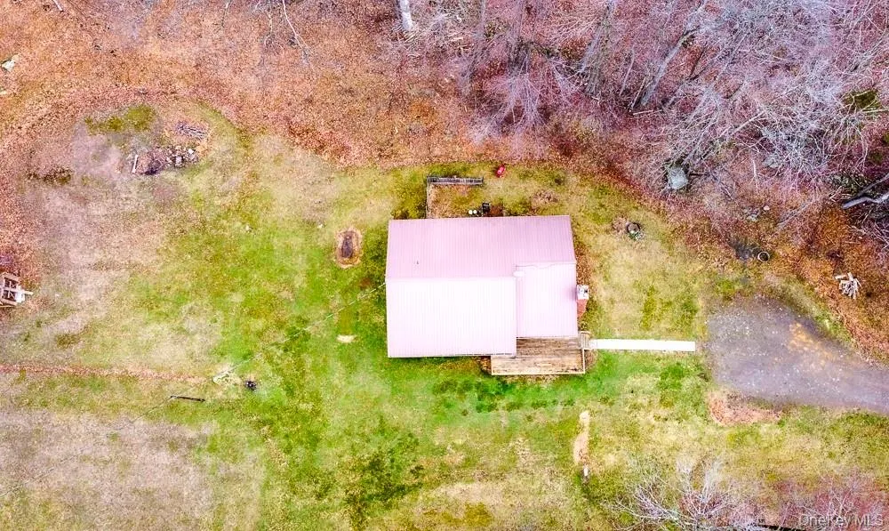 Aerial view of the property featuring a building with a red roof, a driveway, and surrounding green and brown foliage Aerial view of the property featuring a building with a red roof, a driveway, and surrounding green and brown foliage