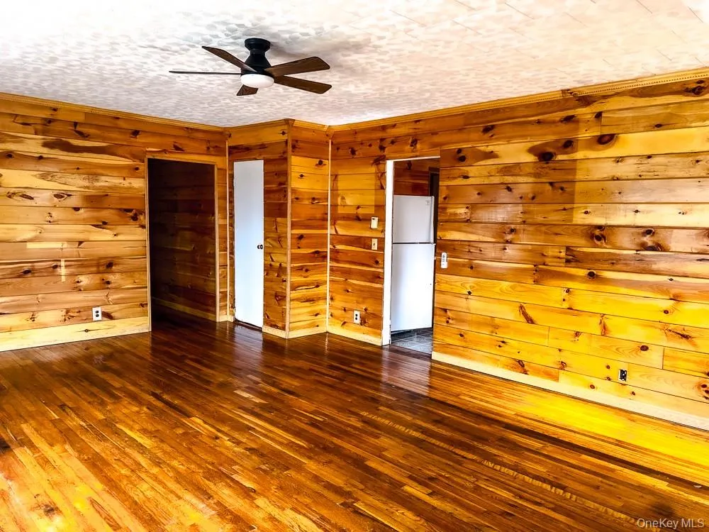 Living space featuring hardwood flooring, wood paneling on the walls, and a ceiling fan with integrated lighting Living space featuring hardwood flooring, wood paneling on the walls, and a ceiling fan with integrated lighting