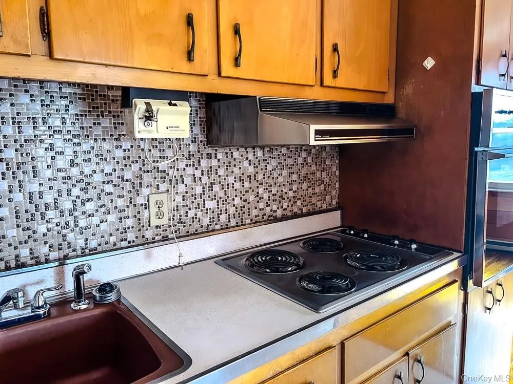 The kitchen features wood cabinetry, a tiled backsplash, a cooktop, and a sink with a chrome faucet The kitchen features wood cabinetry, a tiled backsplash, a cooktop, and a sink with a chrome faucet
