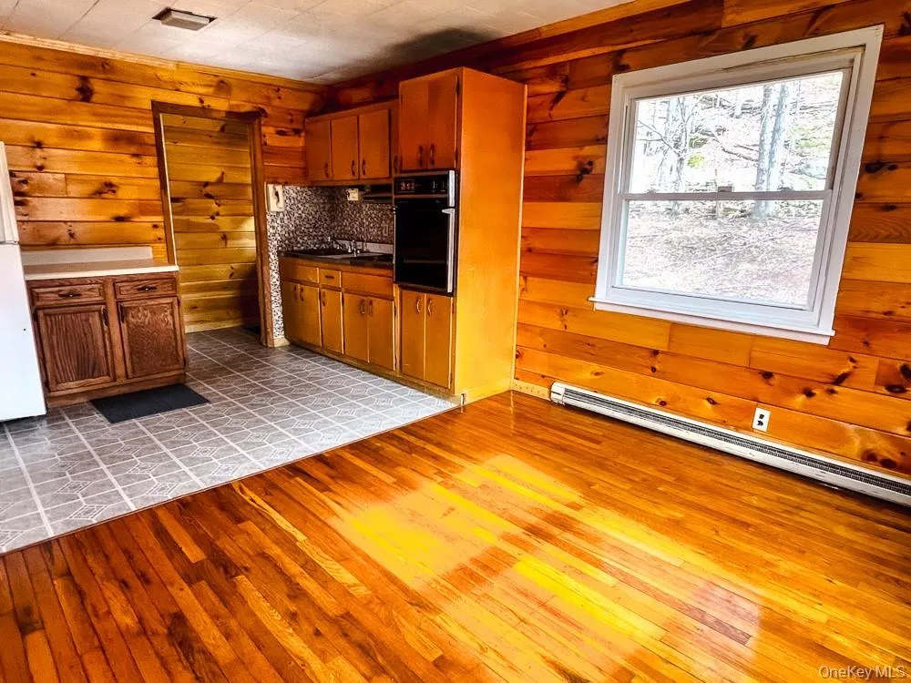 This kitchen features wood paneling, a window providing natural light, and a mix of hardwood and tiled flooring This kitchen features wood paneling, a window providing natural light, and a mix of hardwood and tiled flooring