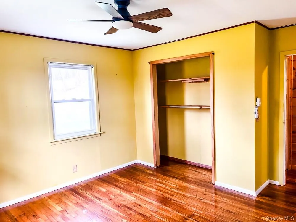 Room featuring hardwood floors, a window providing natural light, a ceiling fan, and a built-in closet with shelving Room featuring hardwood floors, a window providing natural light, a ceiling fan, and a built-in closet with shelving