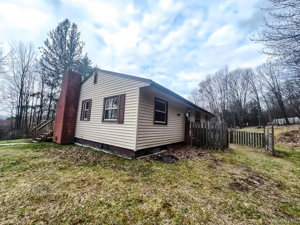 The property features light-colored horizontal siding, dark window shutters, and a prominent brick chimney The property features light-colored horizontal siding, dark window shutters, and a prominent brick chimney